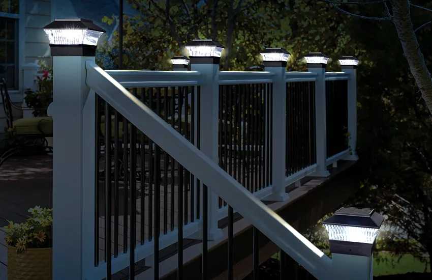 Solar-powered LED post cap lights on black balusters with white railing at dusk