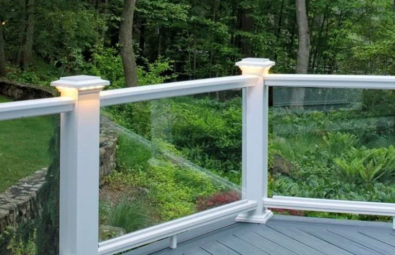 Tempered glass panel railing with white composite posts and LED post cap lights overlooking wooded yard